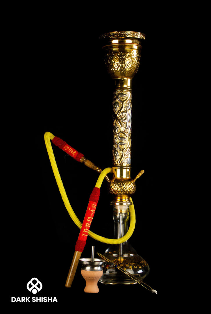 Narghilè Tradizionale Tutankhamon da 90 cm, realizzato in ottone con ricami orientali e dotato di tubo in pelle e legno. Completo di tutti gli accessori, con design artigianale e sistema a camera chiusa per un’esperienza di fumo autentica.